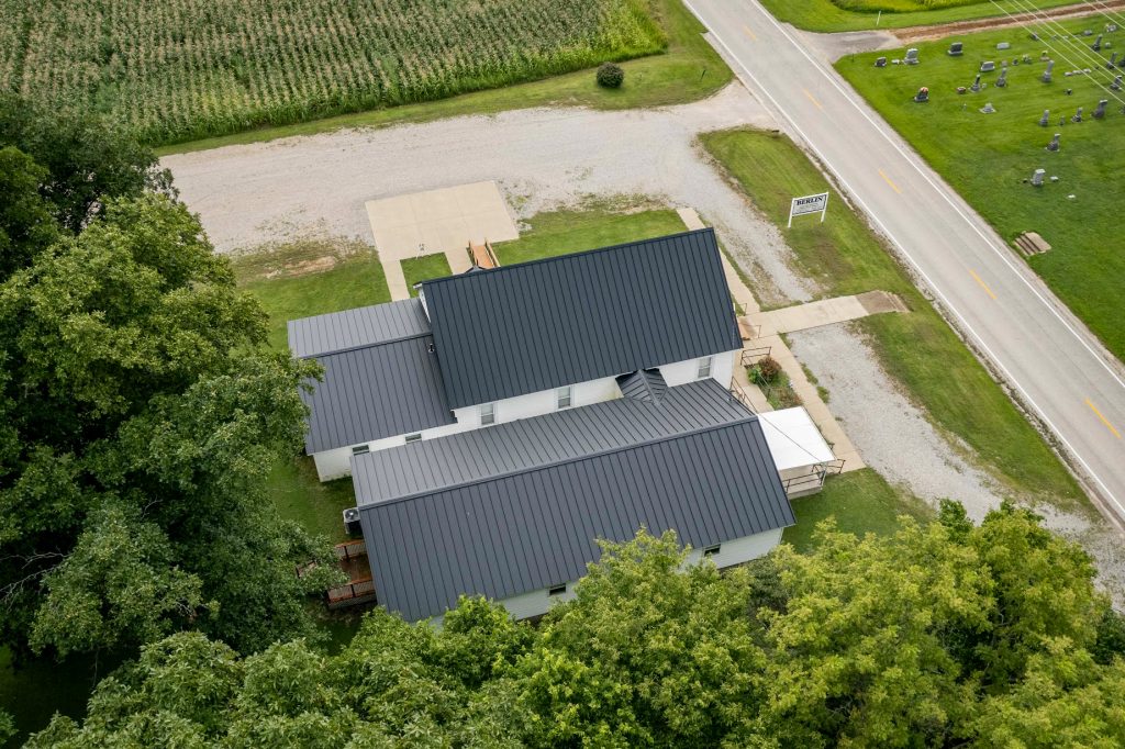 Bird's-eye view of a church with a black roof, showcasing its position in a scenic agricultural area.