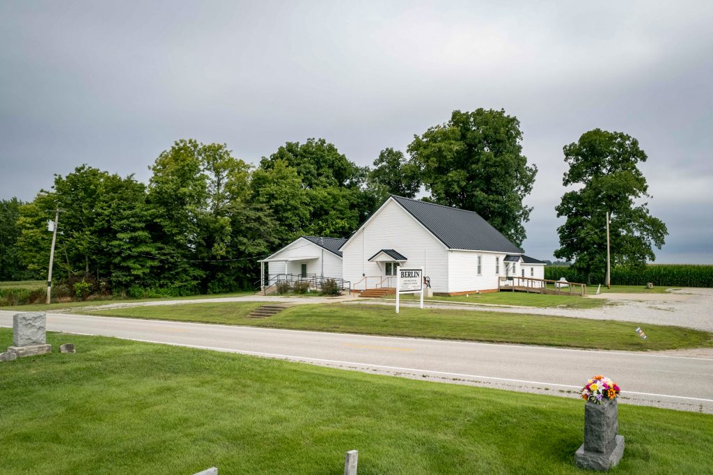 A white church featuring a standing seam roof, with a cemetery visible in the foreground.
