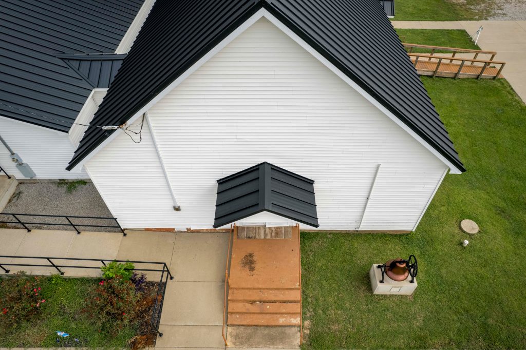 Aerial perspective of a white church with a black roof, showcasing its standing seam design amidst the landscape.