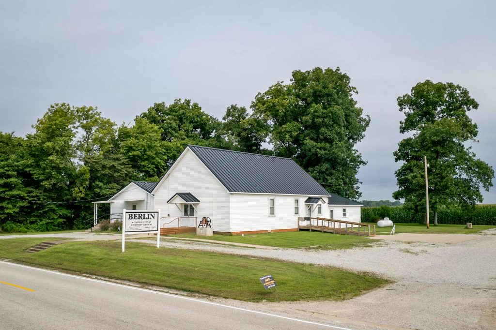 A white church featuring a black standing seam roof and a prominent sign.