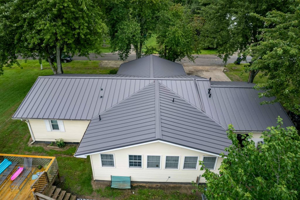 Aerial view of a house featuring a standing seam metal roof, showcasing its sleek design and surrounding landscape.