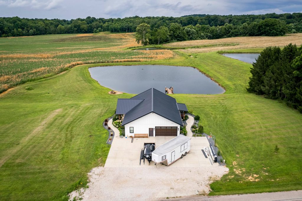 A house with a standing seam roof and a pond set in a rural landscape.