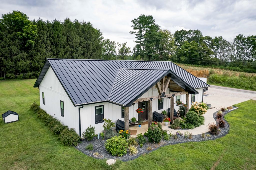 A house featuring a black standing seam roof surrounded by a large green yard.