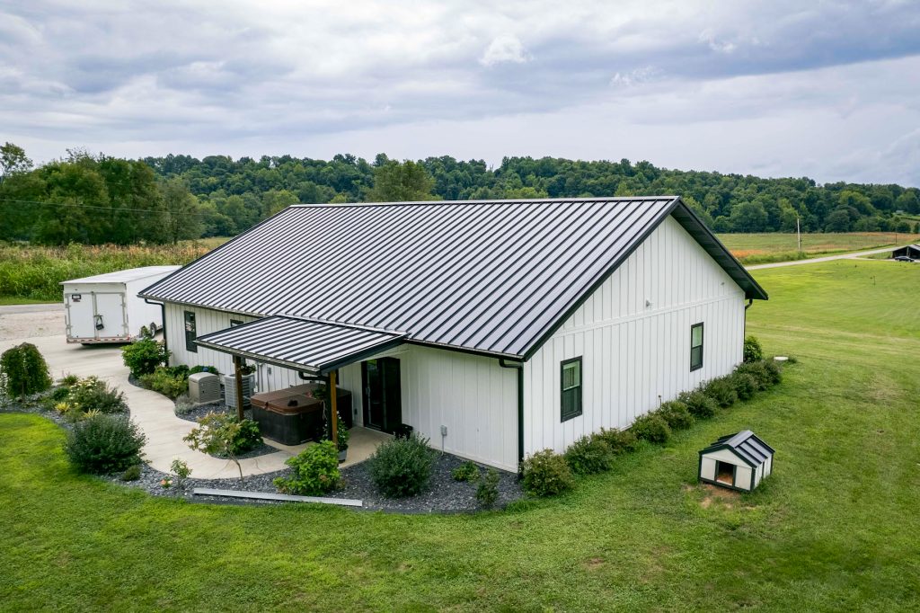 A house with a standing seam metal roof and a nearby dog house in a countryside landscape.