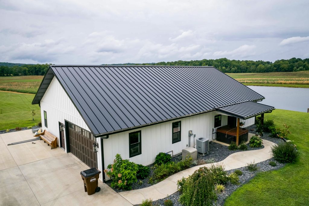 A house featuring a standing seam metal roof, accompanied by a well-maintained driveway.