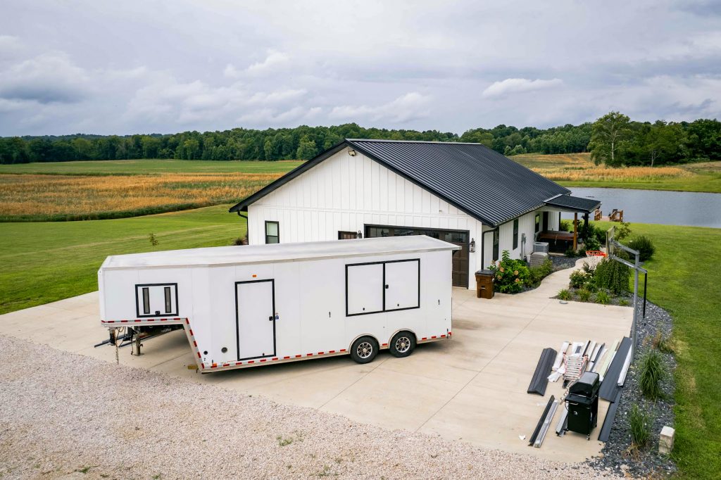A trailer parked in front of a house with a standing seam roof, showcasing a residential setting.