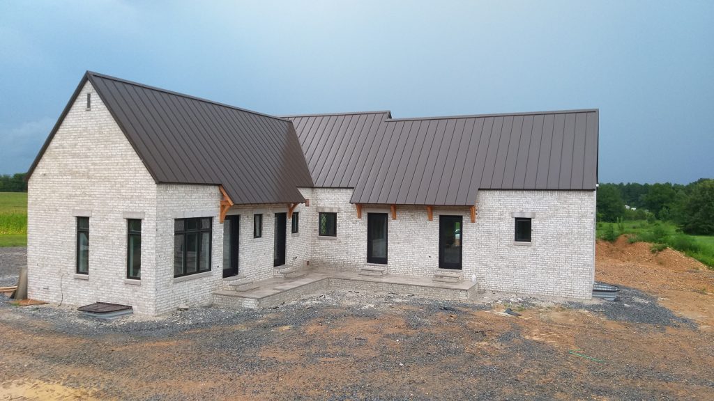 Modern farmhouse with white brick exterior and bronze standing seam metal roof with cedar bracket accents
