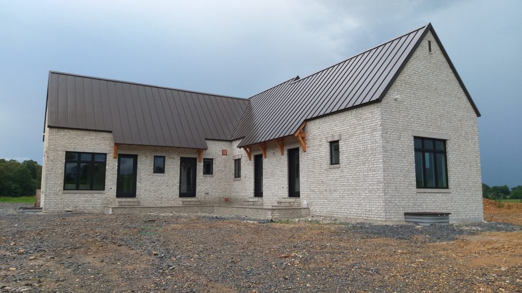 Side view of white brick farmhouse featuring bronze standing seam metal roof with multiple gabled sections