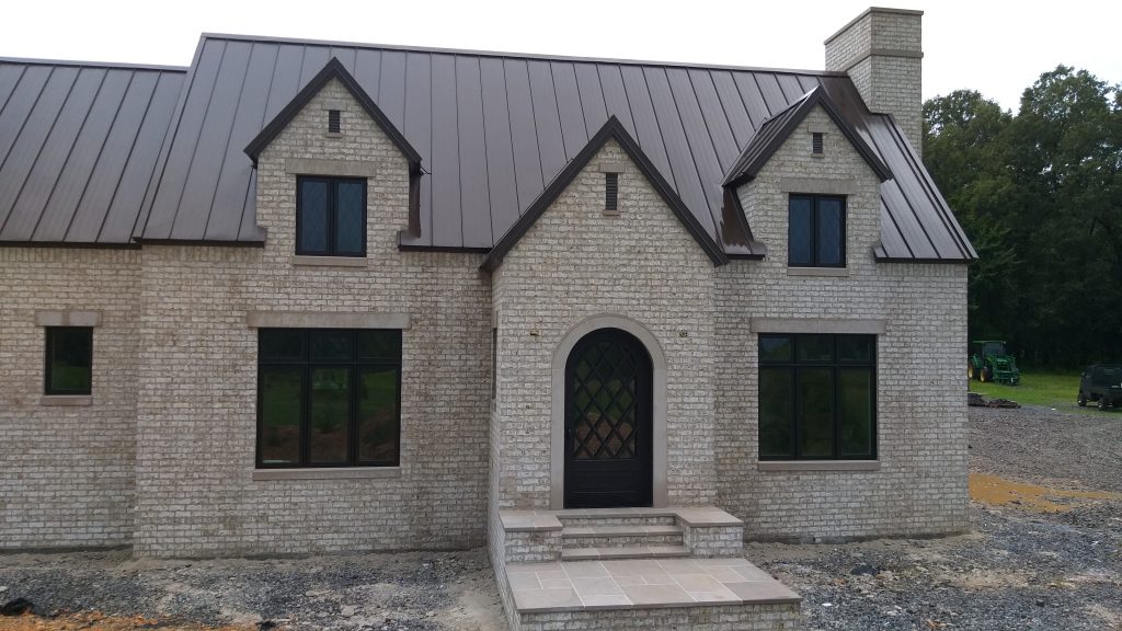 White brick home featuring bronze standing seam metal roof with multiple gabled dormers and brick chimney