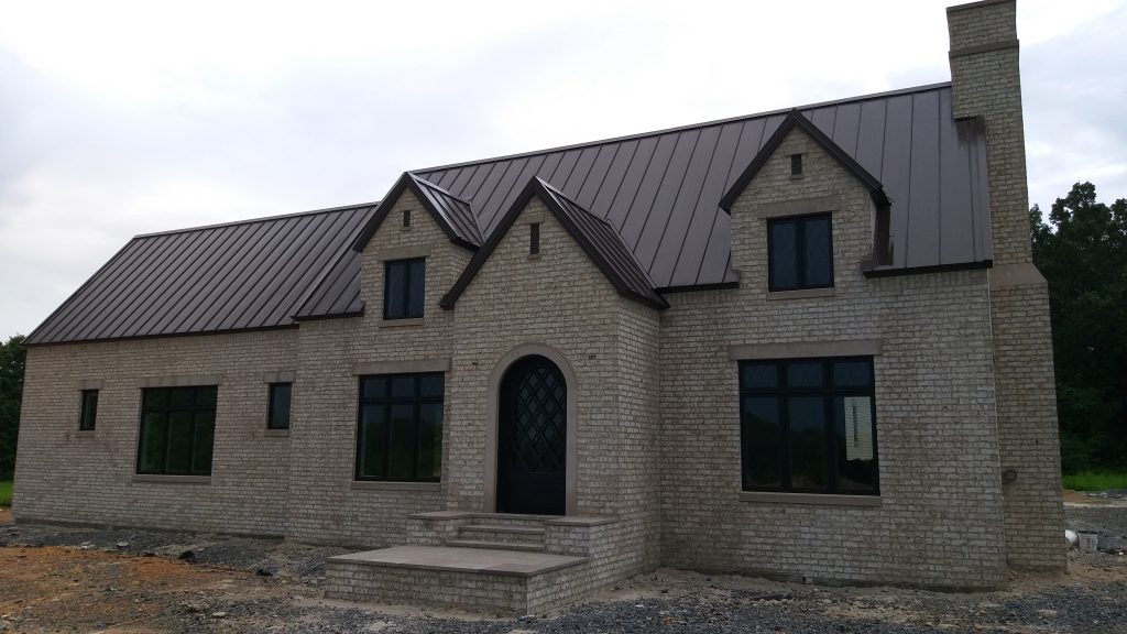 White brick Tudor-style home with bronze standing seam metal roof and arched entry door