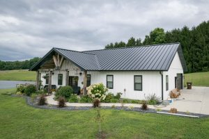 A home with a large porch featuring white metal siding and black metal standing seam roofing installed by Kingdom Home Exteriors in central Illinois.