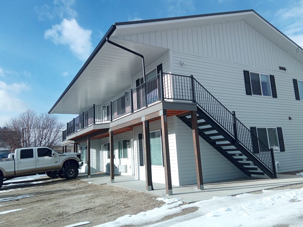 Two-story residential building with Alamo White Crinkle textured metal siding and black metal railings on wrap-around deck