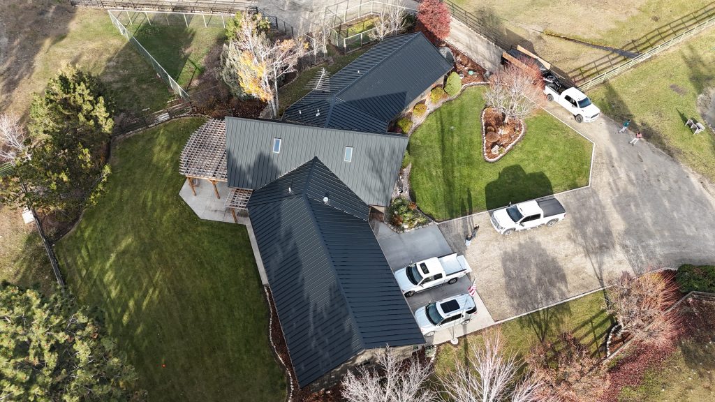 Aerial view of home with black Crinkle metal roof and coordinating dark standing seam metal siding surrounded by autumn foliage