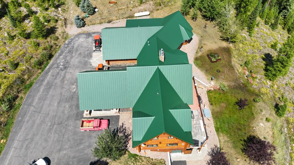 Drone view of home with hunter green standing seam metal roof on wooded property with access drive