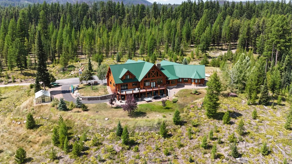 Wide aerial view of log home with hunter green metal roof nestled in expansive mountain pine forest
