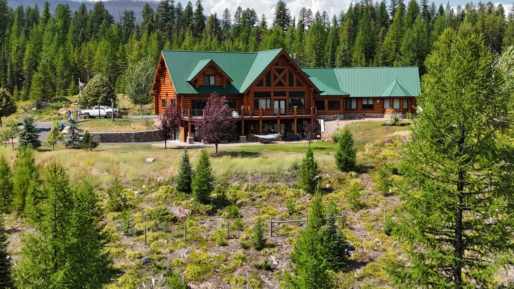 Log home featuring hunter green standing seam metal roof with mountain forest backdrop