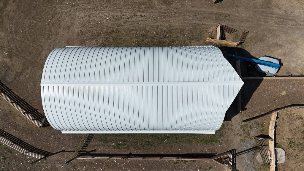 Top-down overhead view of white curved standing seam metal roof on equestrian barn structure