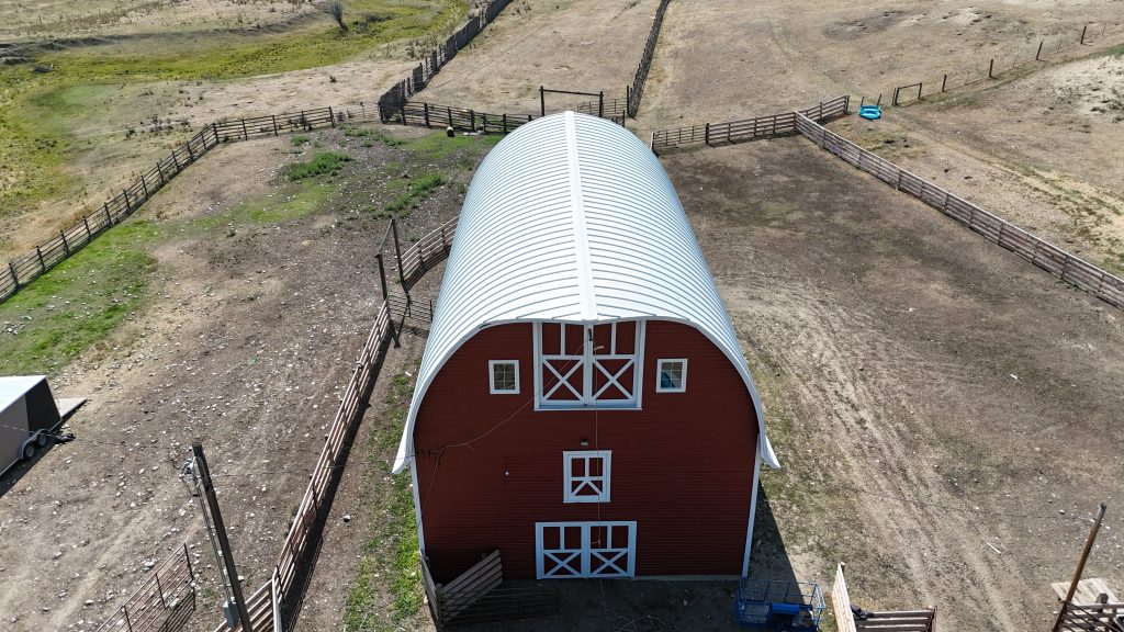 Overhead aerial view of white curved arched metal roof on traditional red barn