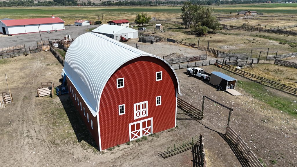 Large red barn featuring white curved arched metal roof with traditional double entry doors