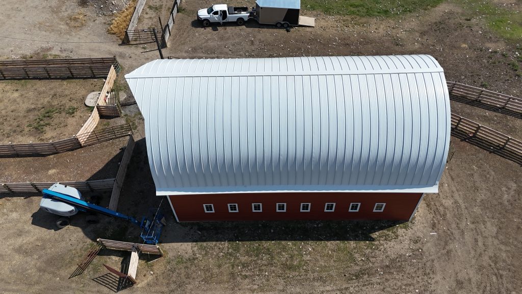 Lengthwise overhead aerial view of red barn with white curved standing seam metal roof
