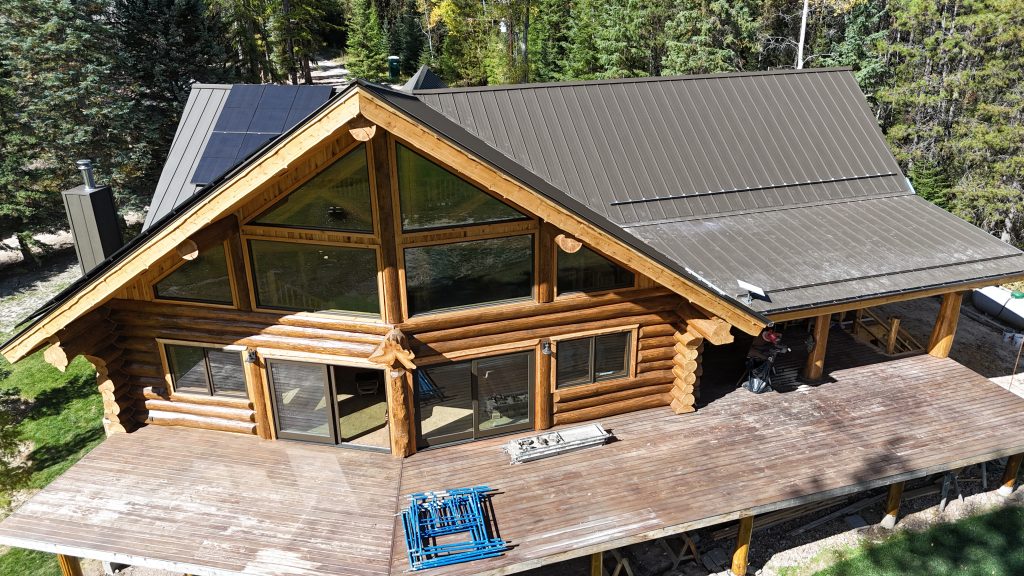 Log home with soaring glass gable end and charcoal standing seam metal roof featuring rooftop solar panels