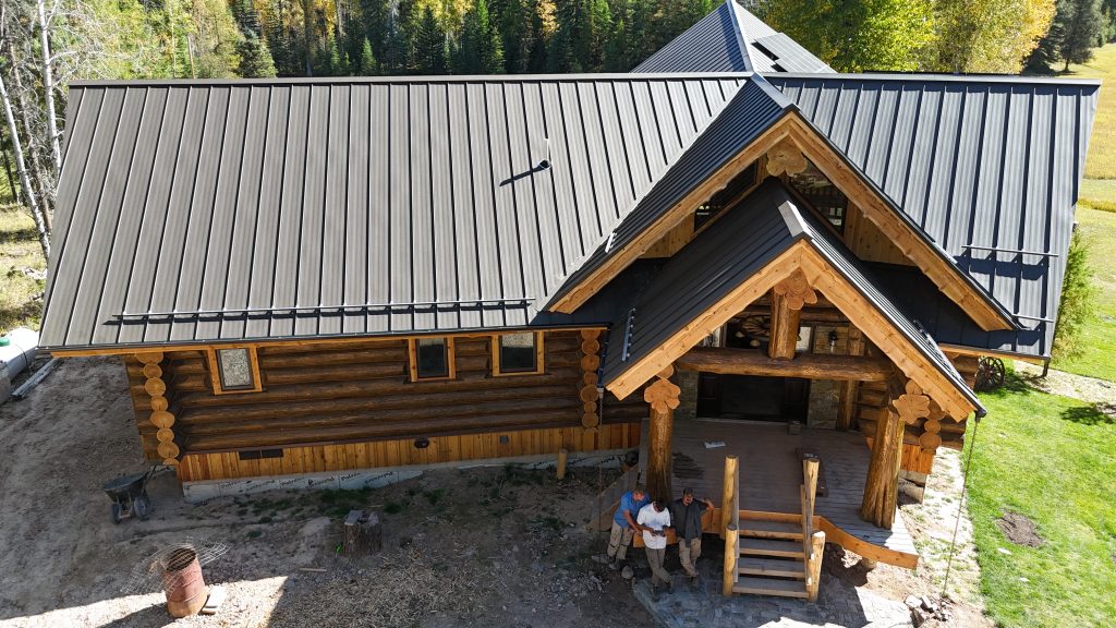Aerial view of log home with charcoal standing seam metal roof during installation phase