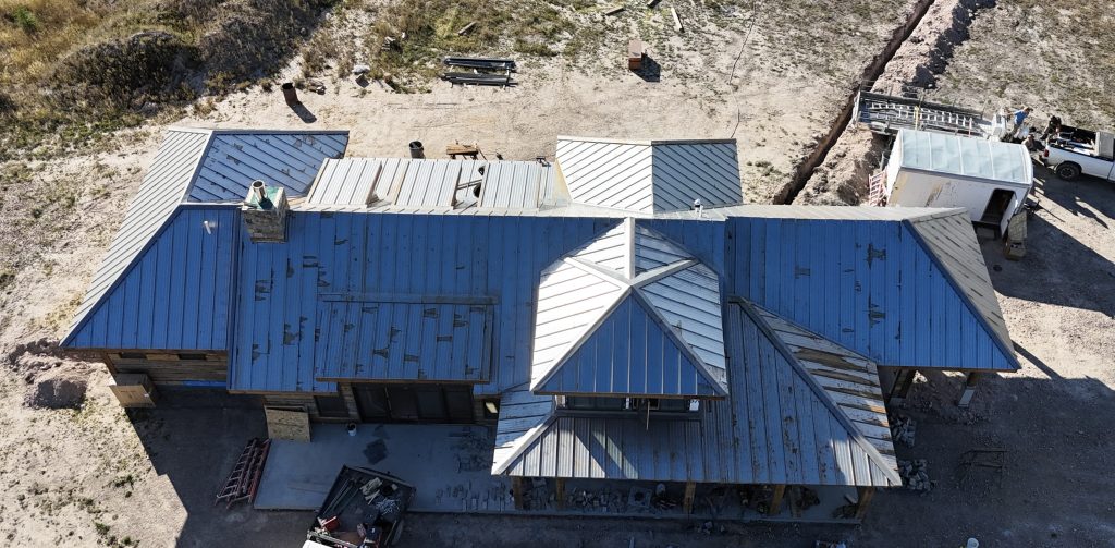 Aerial view of residential metal roof installation in progress with newly placed standing seam panels