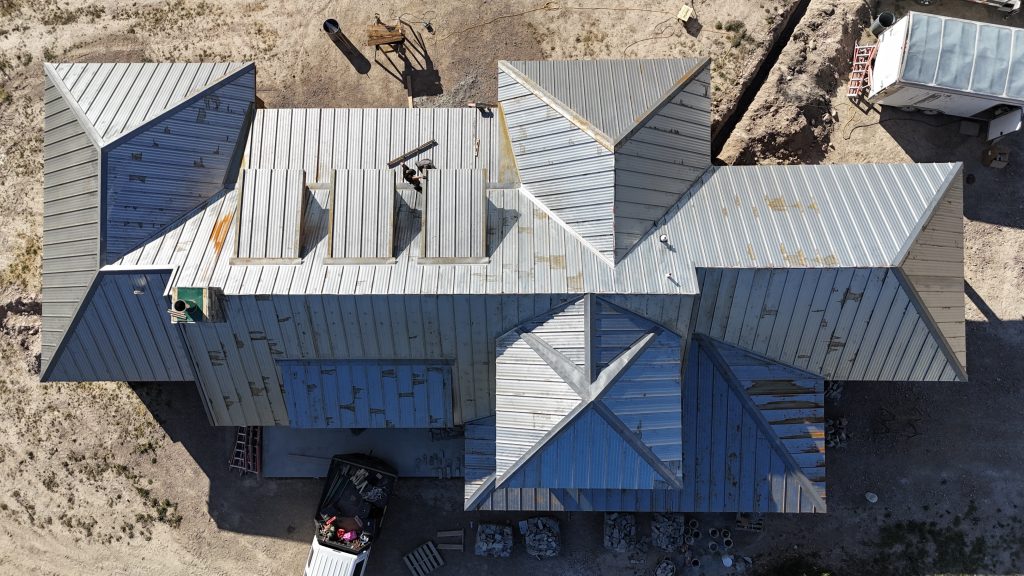 Overhead view of metal roof installation showing roofing panels being laid across complex roofline