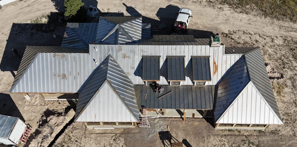Roofing crew installing standing seam metal roof panels on large residential home with dormers