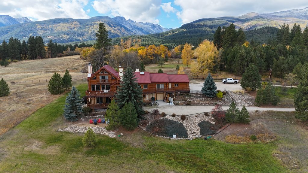 Log home with Rustic Red metal roof set in mountain valley with autumn aspens and evergreen forest