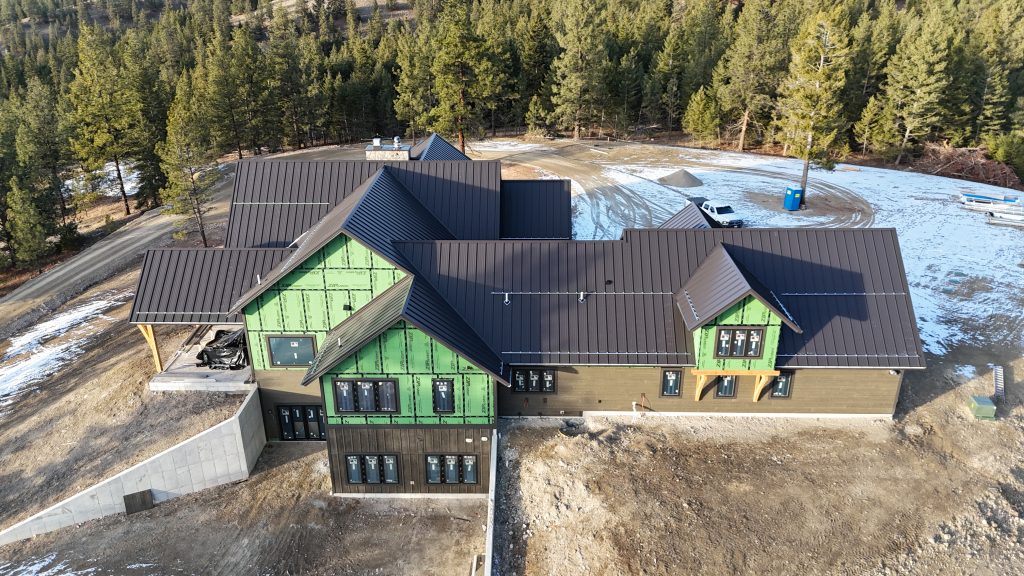 Metal roof installation on custom home under construction with exposed ZIP sheathing walls