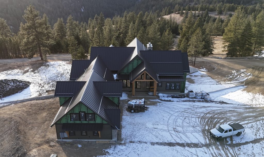Aerial view of new construction home with installed dark metal roof and timber frame entry porch