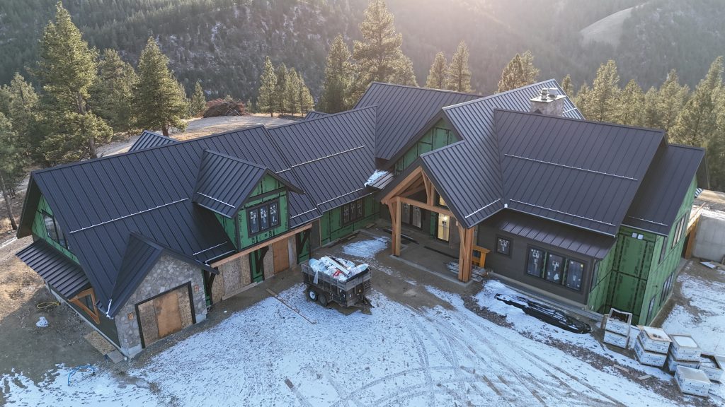 Custom mountain home under construction featuring completed dark standing seam metal roof system
