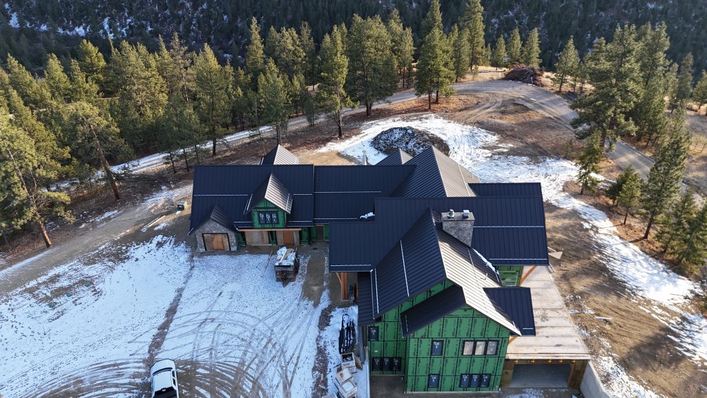 Aerial view of custom mountain home with dark metal roof and substantial timber frame entry