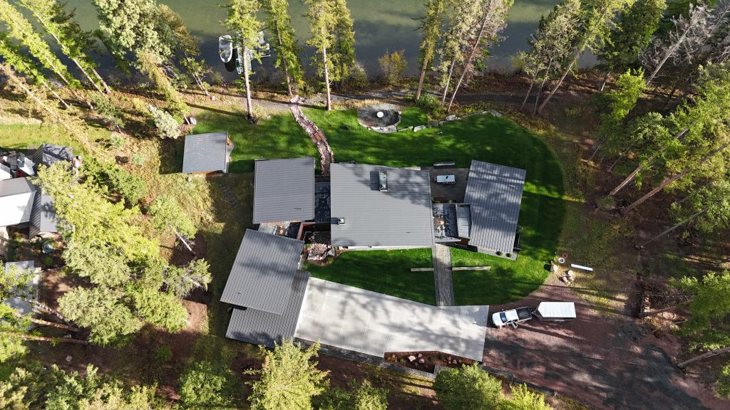 Overhead aerial of lakefront home with charcoal standing seam metal roof surrounded by tall pines