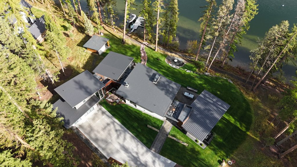 Aerial view of modern lakefront home with charcoal metal roof and private boat dock on lake
