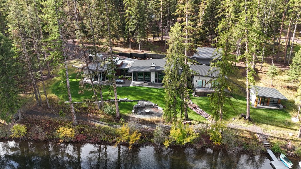 Wide aerial view of lakefront estate with charcoal metal roof nestled among tall ponderosa pines