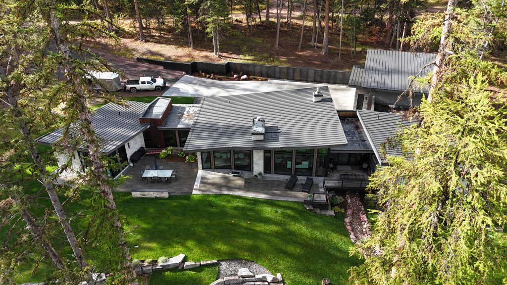 Modern architectural home with charcoal standing seam metal roof stone exterior and paver patio dining area
