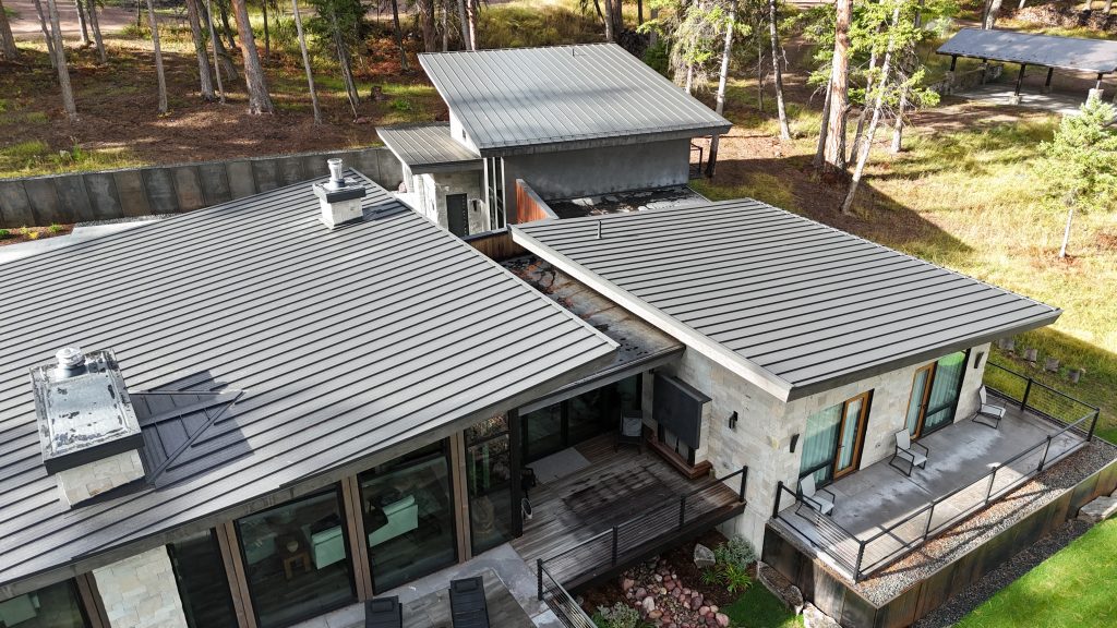 Angled aerial of modern home with charcoal metal roof showing stone walls and connecting roof sections