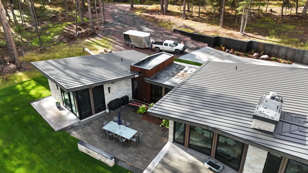 Wide aerial view of modern home with multi-section charcoal metal roof nestled in forest setting