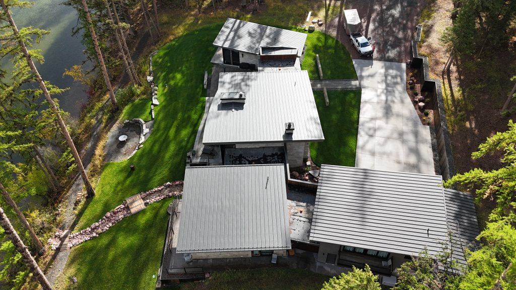 Elevated aerial of modern home with charcoal metal roof on forested waterfront property