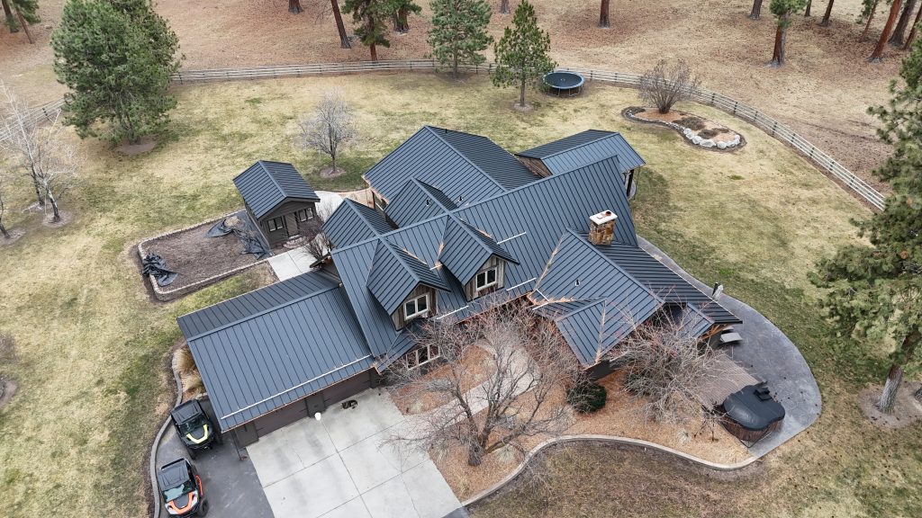 Aerial view of large residential home with black standing seam metal roof and multiple gabled sections