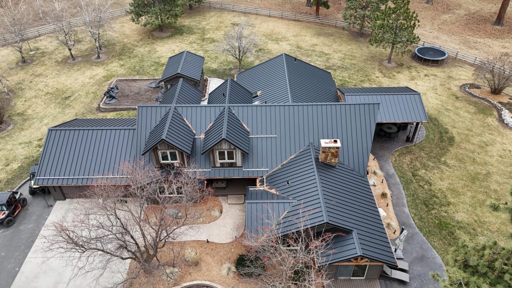 Aerial view of home with black metal roof featuring dormers complex roofline and covered patio