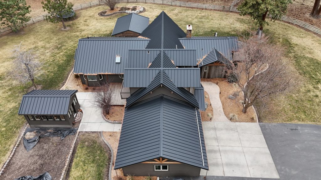 Aerial view of complex ranch home with charcoal metal roof featuring multiple gables and detached sunroom