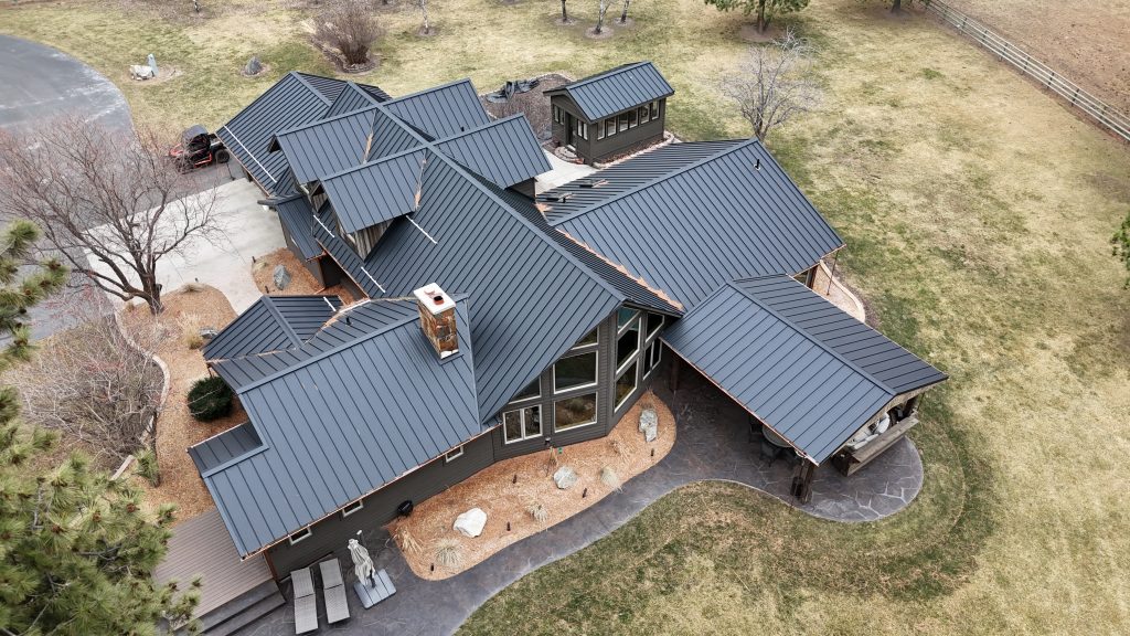 Overhead aerial of large ranch home with intricate charcoal metal roof system and stone chimney