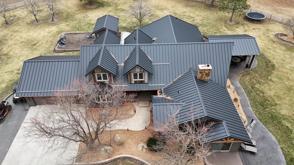 Wide aerial of large ranch home with charcoal metal roof showing full property with multiple roof sections