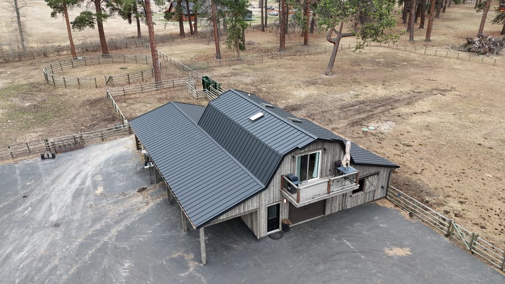 Barndominium with charcoal standing seam metal roof and upper balcony on working ranch with corrals