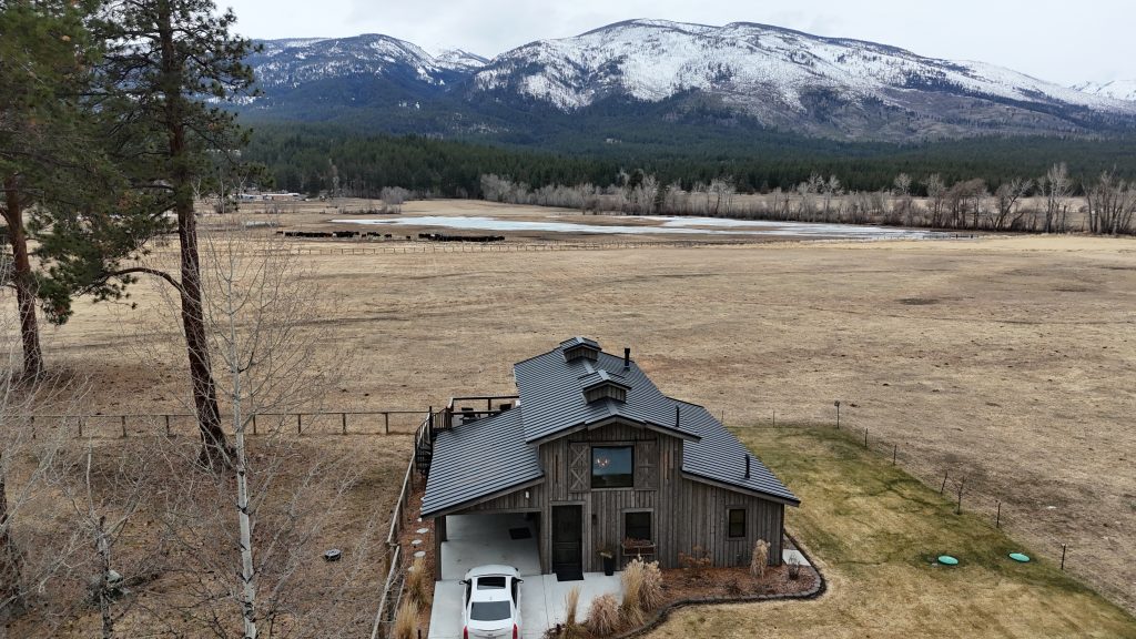 Barndominium with charcoal standing seam metal roof overlooking cattle ranch and snow-capped Montana mountains