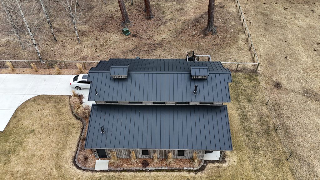 Overhead aerial of charcoal standing seam metal roof on weathered wood barndominium with rooftop deck