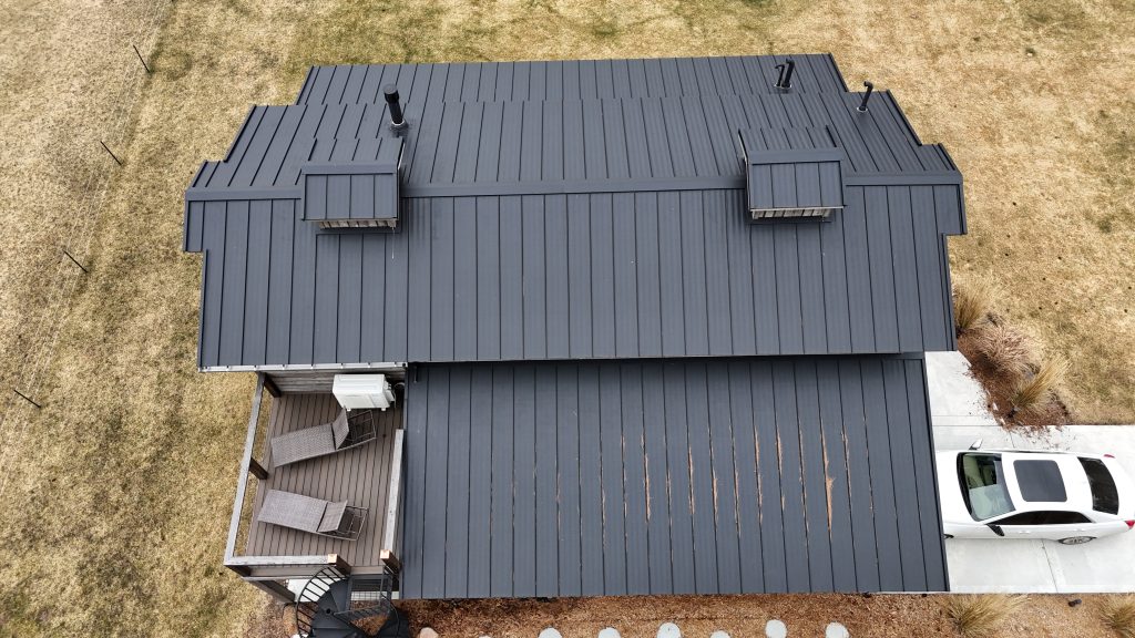 Close overhead aerial showing charcoal standing seam metal roof panels and rooftop deck on barndominium